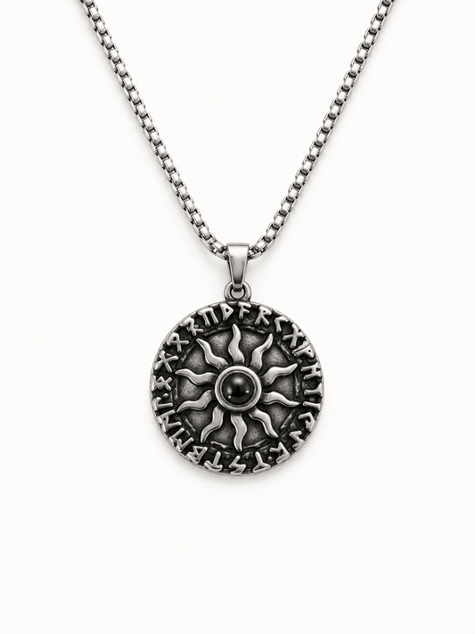 A silver-toned necklace featuring a circular pendant with an embossed sunburst design and raised lettering around the edge, suspended from a matching box chain against a plain white background.