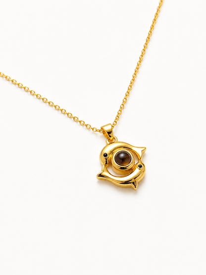 A gold pendant necklace featuring a stylized fish or dolphin shape with a brown circular stone set in the center, shown on a clean white background.