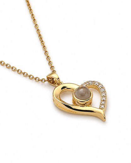Gold heart pendant necklace with a central round gray stone and a curved row of small clear stones on one side, shown on a white background.