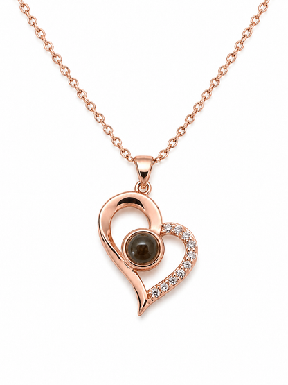 A rose gold heart-shaped pendant necklace featuring a central dark brown gemstone and a curved side adorned with small clear crystals, shown on a white background.
