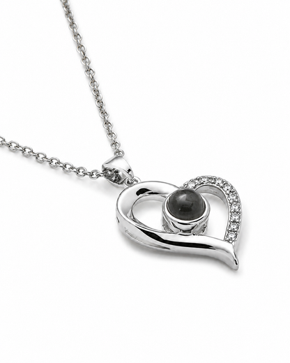 A silver heart-shaped pendant necklace featuring a central dark gray stone and a curved halo of small clear crystals, shown on a white background.