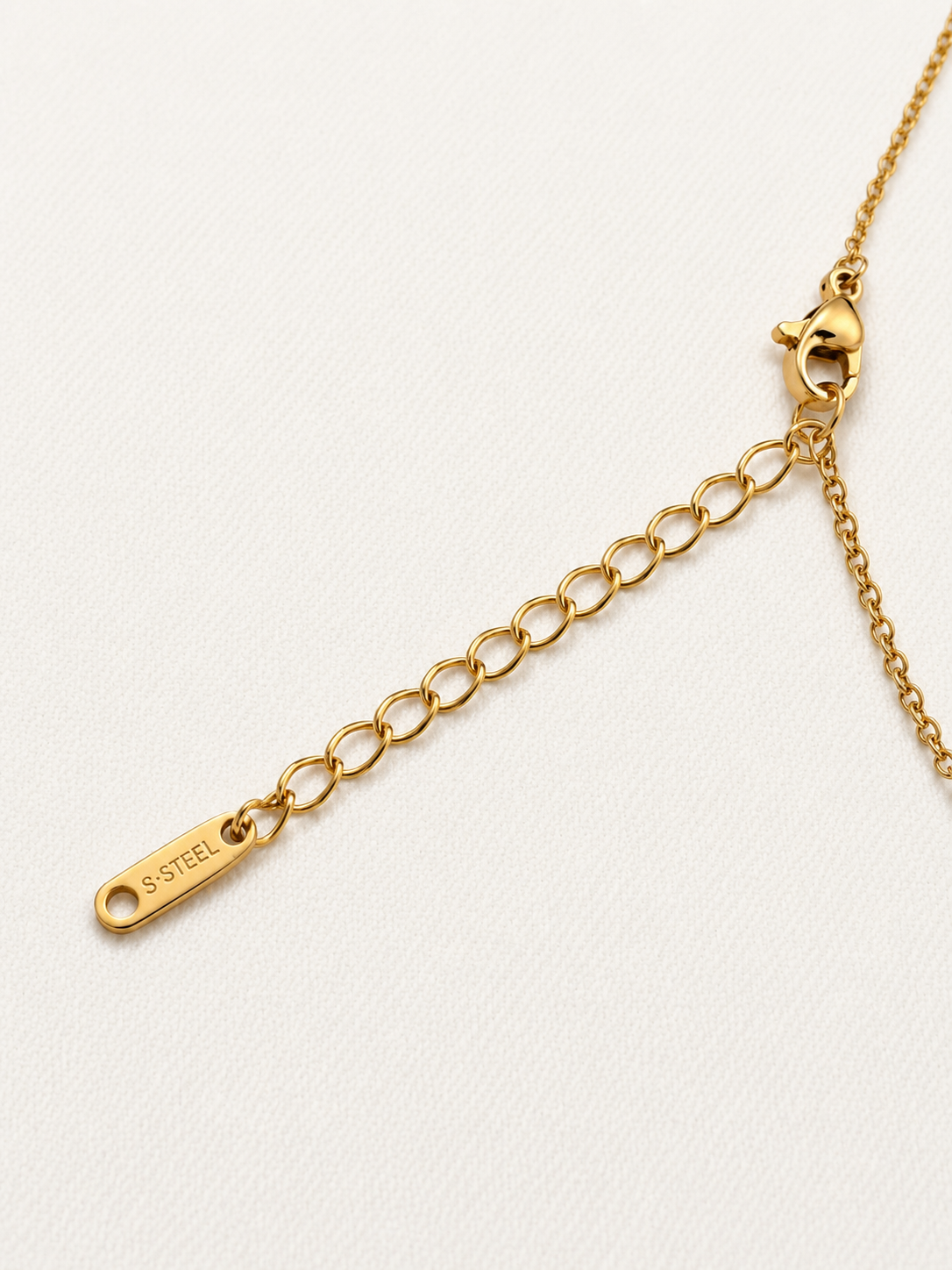 Close-up of a gold chain extender with a lobster clasp and a small engraved tag reading S.S.