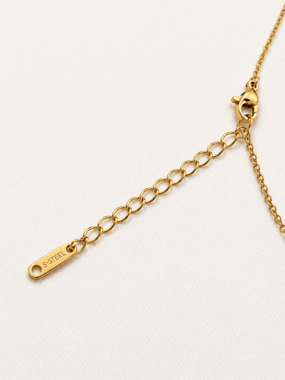 Close-up of a gold chain extender with a lobster clasp and a small engraved tag reading S.Steel.